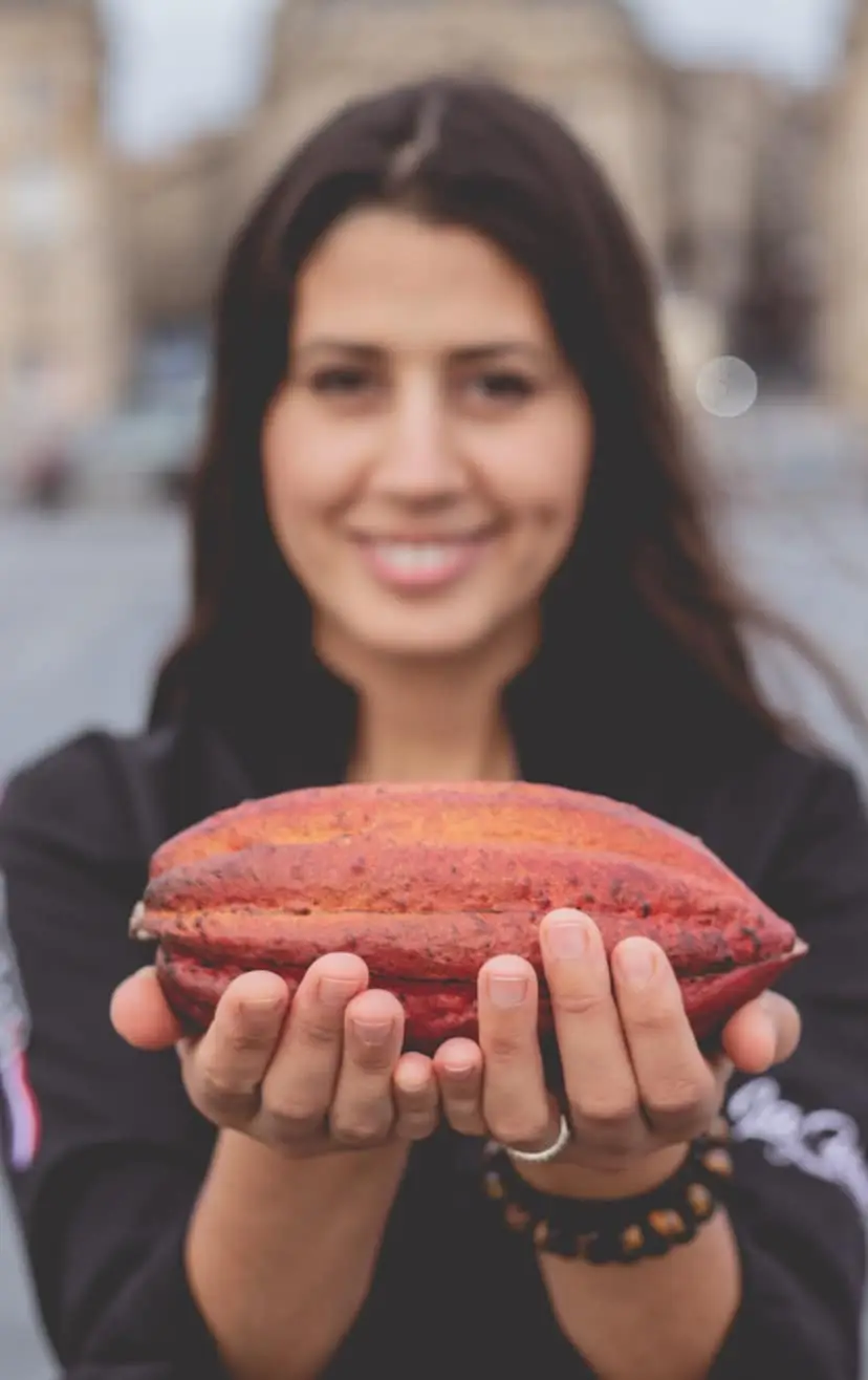 Cette image présente Hasnaâ Ferreira, artisan chocolatier à Bordeaux. Elle tient une cabosse dans ses main